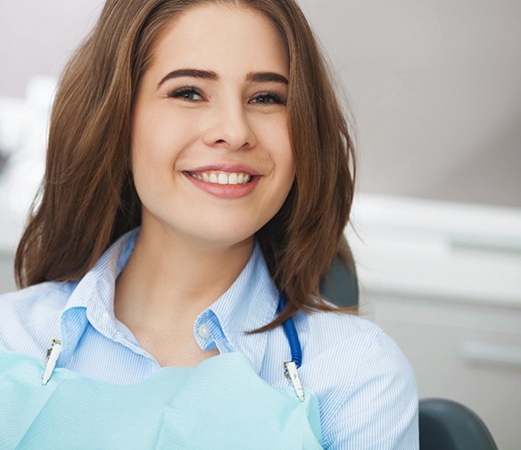 Woman smiling while sitting in dental chair wearing blue shirt